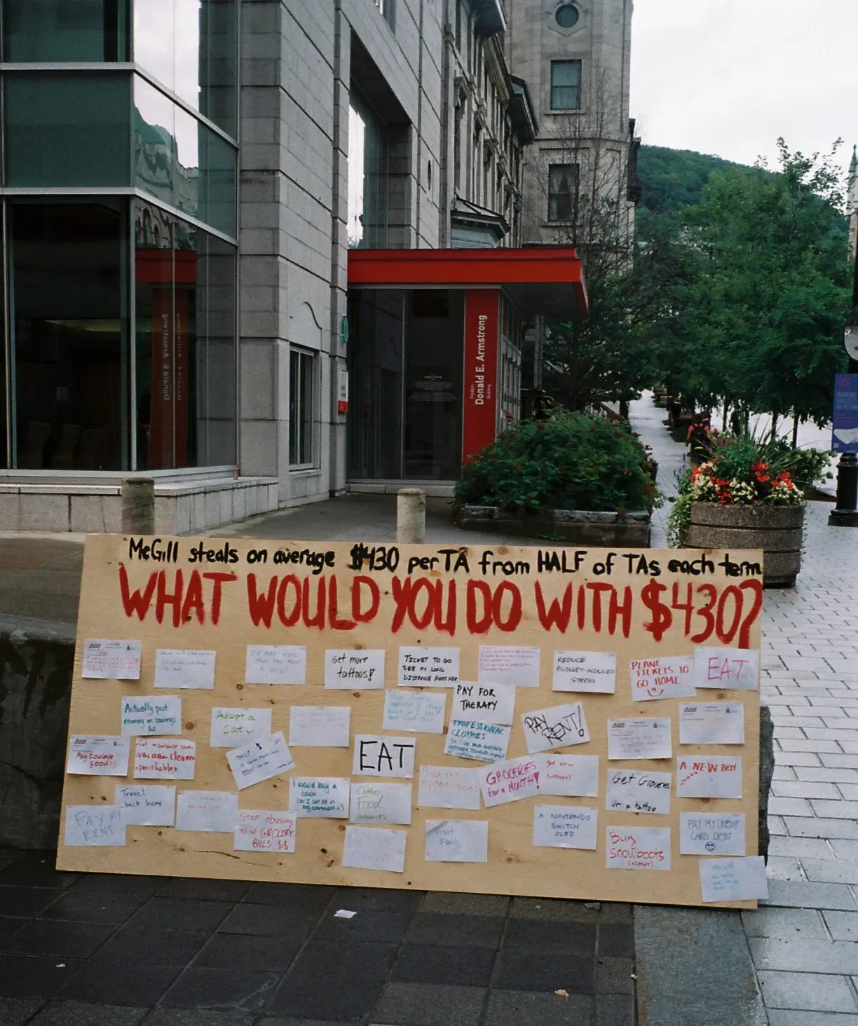 Photo de la planche de bois “What would you do with $430?” où les membres de l’AÉÉDEM pouvait indiqué ce qu’ils feraient avec 430$, incluant les épiceries, payer son loyer, rembourser ses dettes, payer pour la thérapie, adopter un animal de compagnie, visiter sa famille, et se faire tatouer, à la manifestation “First Day of School: Let’s Work to Rule” (August 30, 2023).